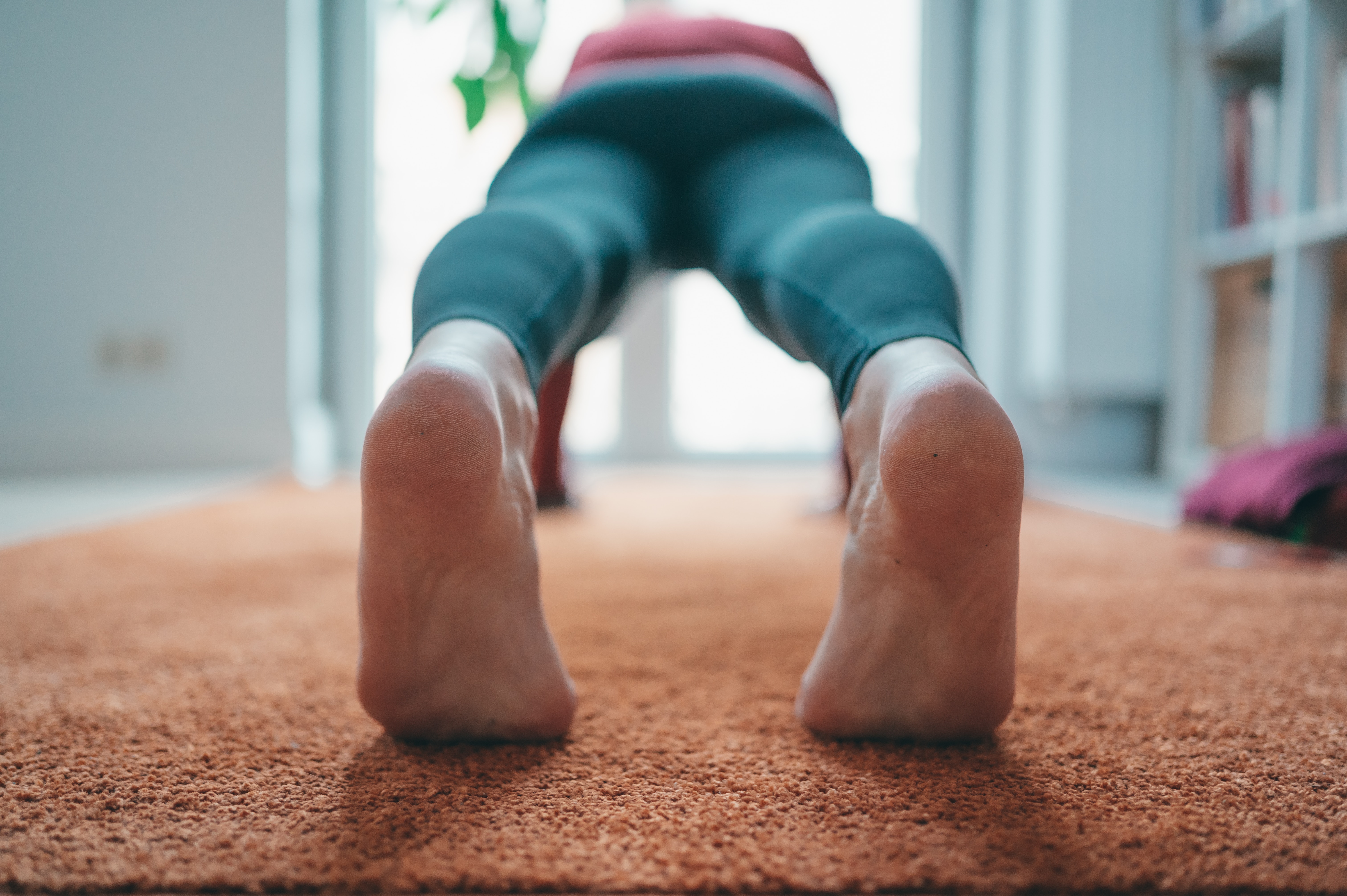 Los pies de una persona en primer plano están sobre una alfombra, practicando yoga o haciendo flexiones.