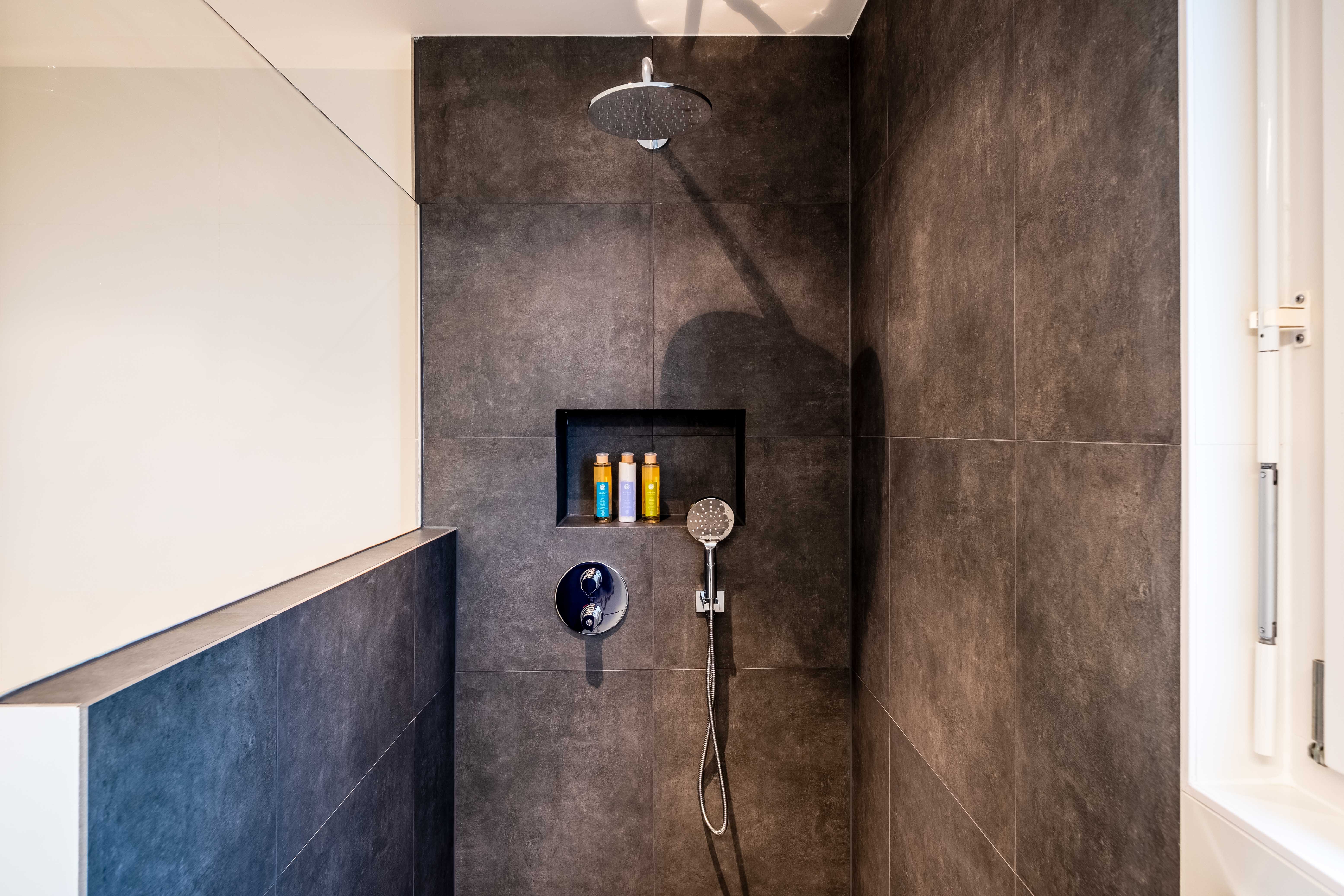 Imagen de una ducha minimalista, en un cuarto de baño moderno con azulejos azules, con presencia de tonos plata oscuro y ámbar oscuro.