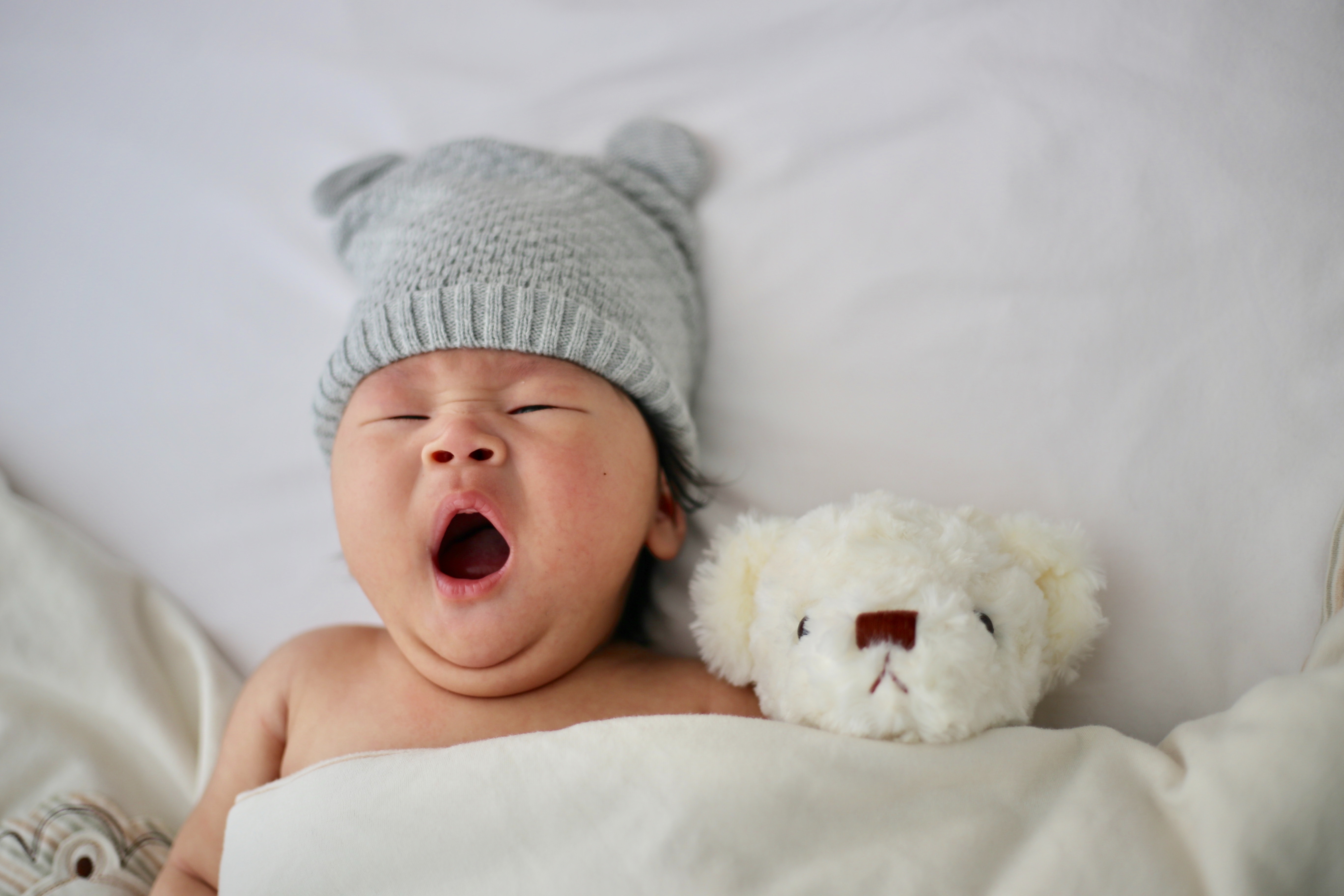 Bebé con gorro de invierno bostezando junto a su peluche